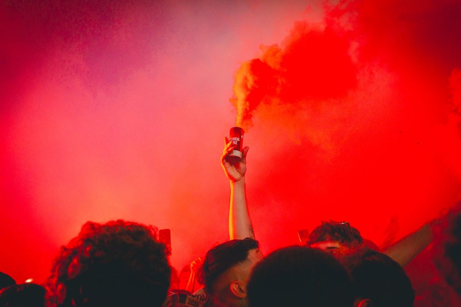 Una mano sostiene un bote de humo sobre la multitud mientras el rojo lo llena todo.