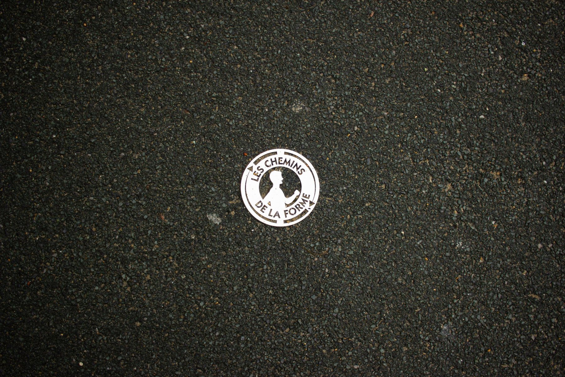 Una placa metálica del recorrido deportivo incrustada en el asfalto.