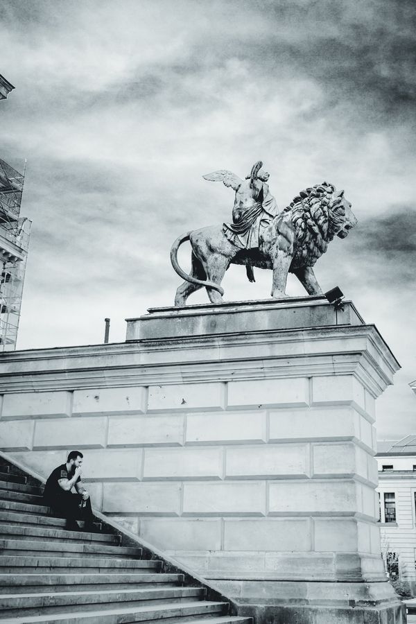 Un hombre descansa en la escalinata de la Konzerthaus mientras la figura alada y su león vigilan desde arriba.