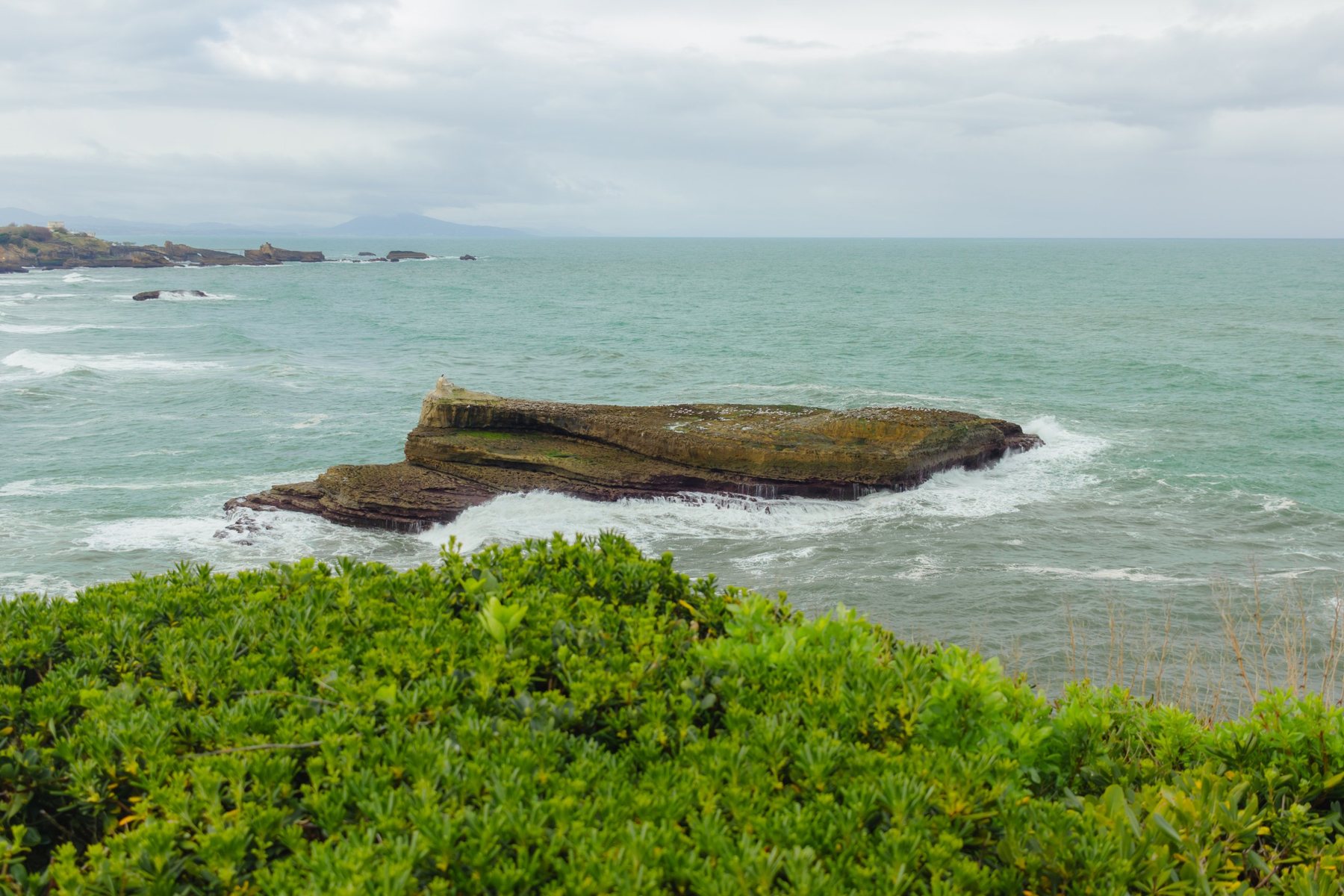 Una roca plana rodeada de espuma, vista desde el acantilado del faro.