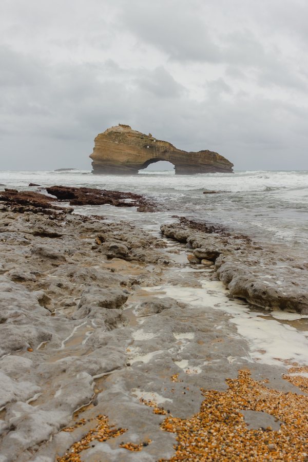 Las losas grises de la playa y la Roche Percée al fondo, entre la espuma.