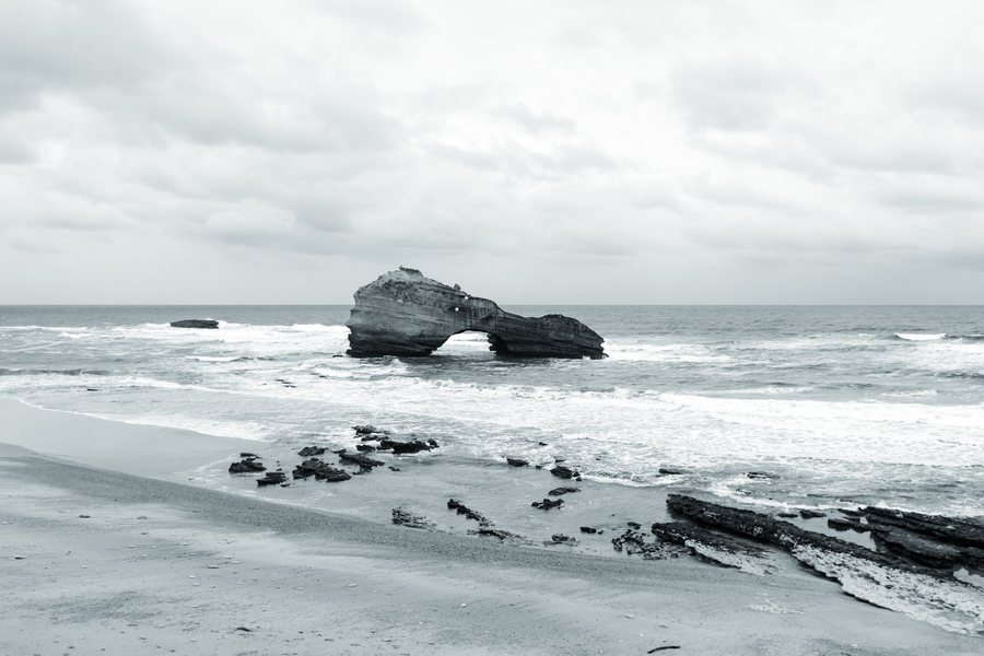 La Roche Percée en el centro del mar revuelto, con la playa y las rocas en primer plano.